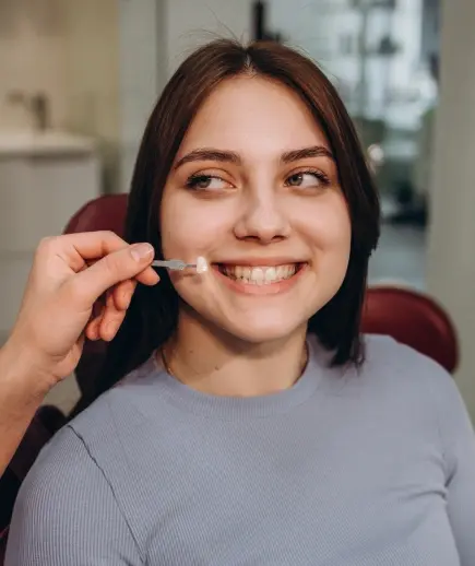 Young woman smiling while holding a dental mirror, showcasing a bright, healthy smile.
