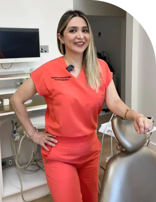 Female dental professional in red scrubs posing in treatment room at Beverly Hills dental practice.
