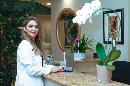 Professional dental receptionist at modern Beverly Hills practice reception desk with plants.